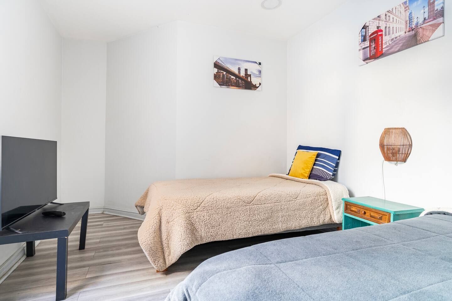 Un dormitorio con cama, televisor, una mesita y una lámpara de pared.