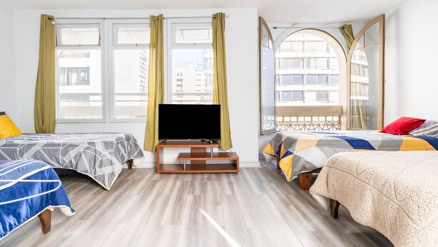 A hotel room with two beds, a TV, and large windows with curtains. - Hostal mancora (Santiago)