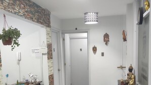 A hallway with a stone wall, a wooden floor, a desk with a plant, a statue, and a heater. - Hostal mancora (Santiago)