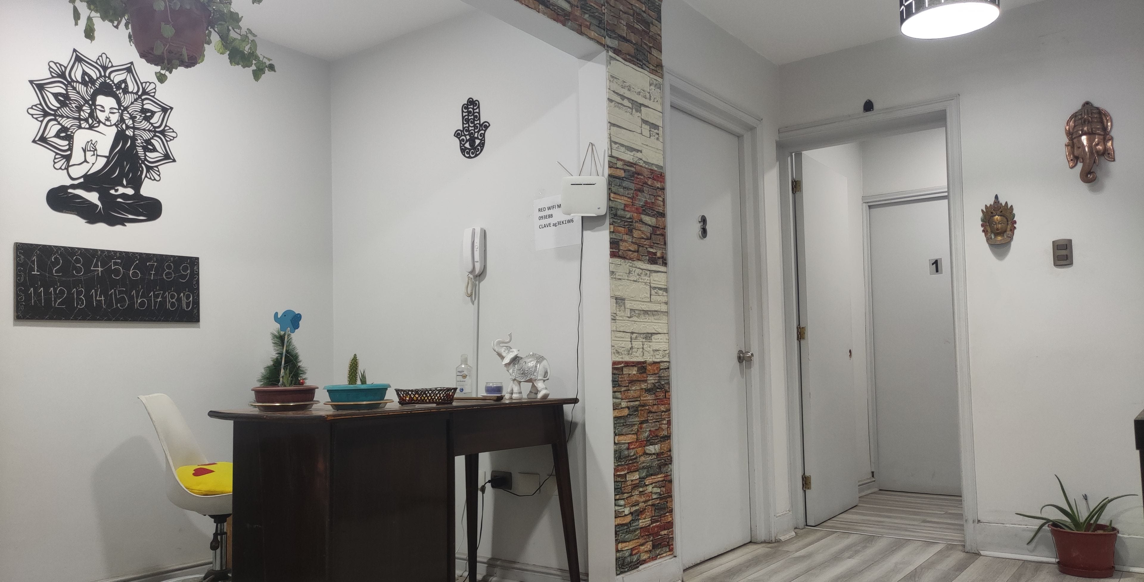 Un pasillo de hotel con piso de madera, un escritorio con planta en maceta, una pared con letrero de número y una puerta.