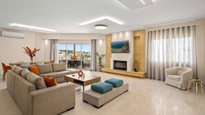 Ein modernes Wohnzimmer mit einer Couch, Poufs, einem Couchtisch, einem Kamin und einem Fernseher.
