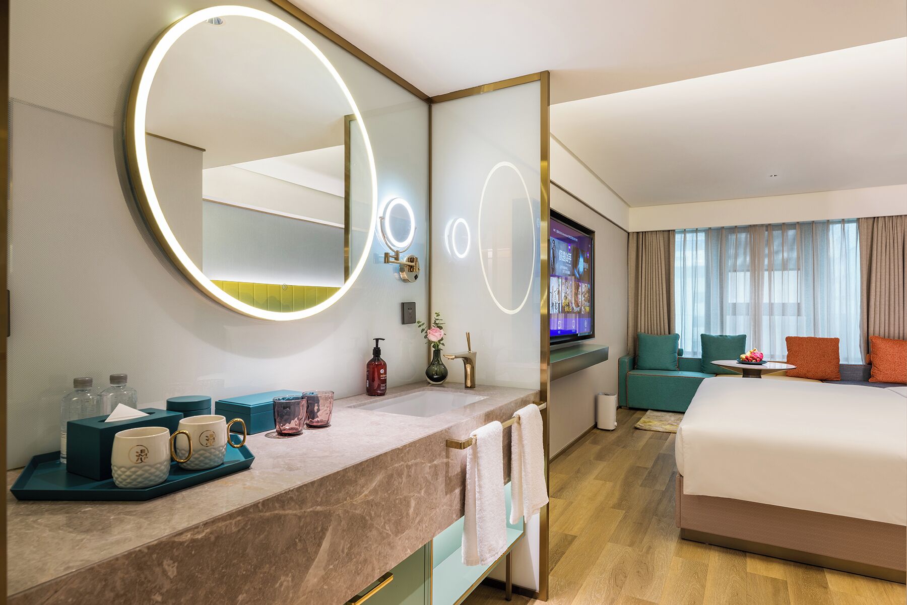 Une chambre d’hôtel avec un grand lit, une télévision, une salle de bain avec un miroir et un coin salon avec une table.