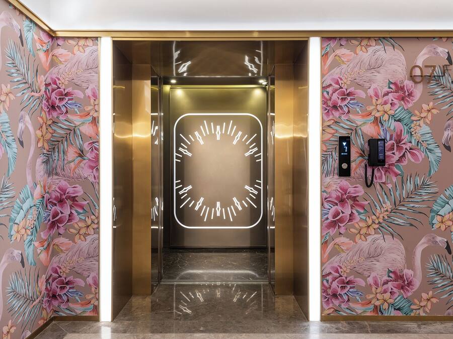 An elevator with a digital clock displaying the time, surrounded by floral wallpaper.