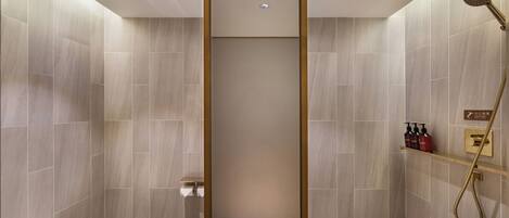 A modern bathroom with a shower, toilet, and a shelf with toiletries.