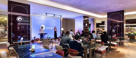 Un salón de conferencias de hotel con escenario, asientos y una zona de bar.