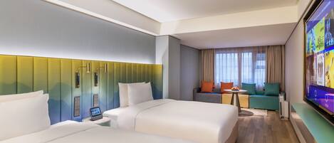 A hotel room with two beds, a television, a sofa, and a desk.