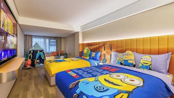 A hotel room with a large bed featuring Minion-themed bedding, a separate seating area with a tent-like structure, and a television on the left side.