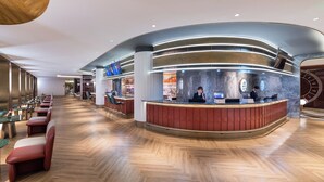 Een moderne hotel lobby met een gebogen receptiebalie, zithoek met tafels en stoelen, en een bar.