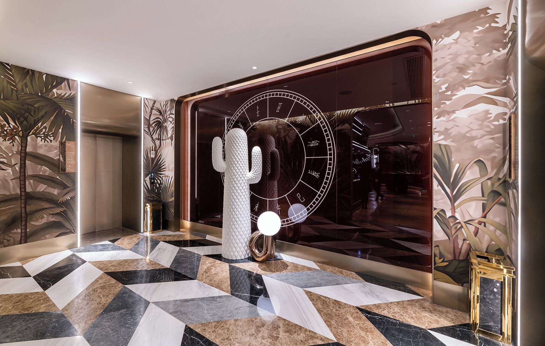Un vestíbulo con piso de diseño geométrico, una gran escultura de cactus y una pared con un reloj y diseño abstracto.