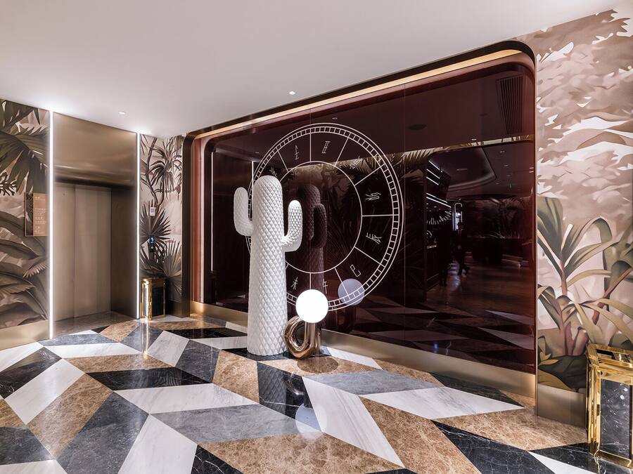 A lobby with a geometric patterned floor, a large cactus sculpture, and a wall with a clock and abstract design.