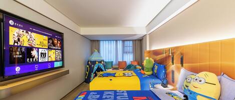 Een hotelkamer met een groot televisiescherm waarop filmopties worden getoond, een bed met een Minion dekbedovertrek en een kindertent.