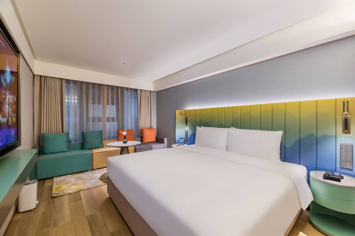 Una habitación de hotel moderna con una cama grande, una zona de estar con un sofá y sillones, una mesita y un televisor.