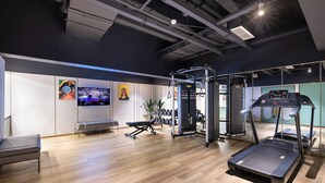A gym with exercise equipment, a bench, and a television on the wall.