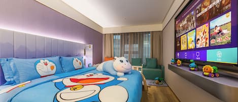 A hotel room with a large bed featuring cartoon character bedding, a television displaying movie posters, and a small shelf with toys.
