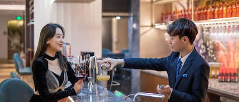 A bar area with a person pouring a drink into a glass. There are shelves with bottles and glasses in the background.