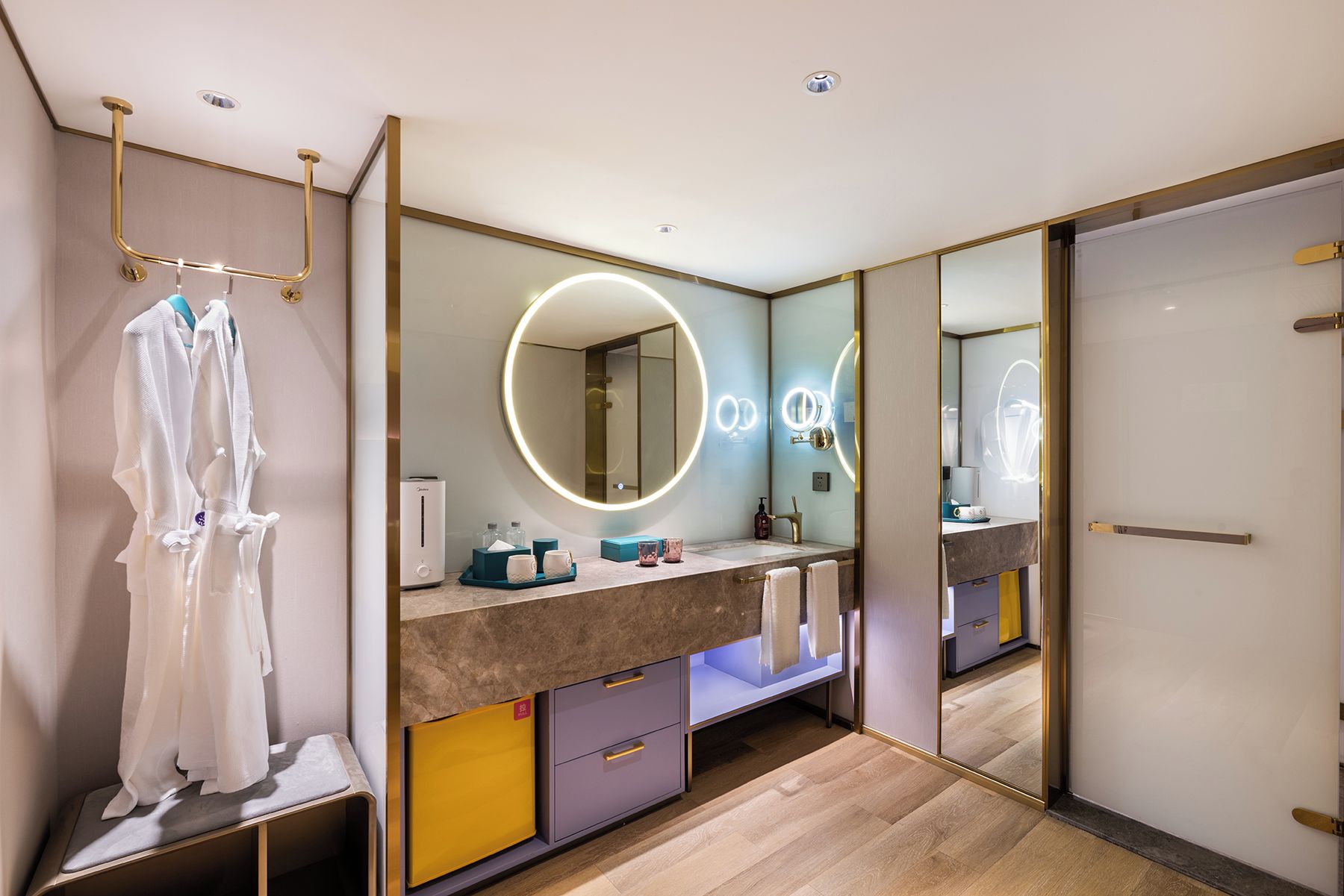 Un baño moderno con tocador, un espejo grande con iluminación circular y un banco con toallas.