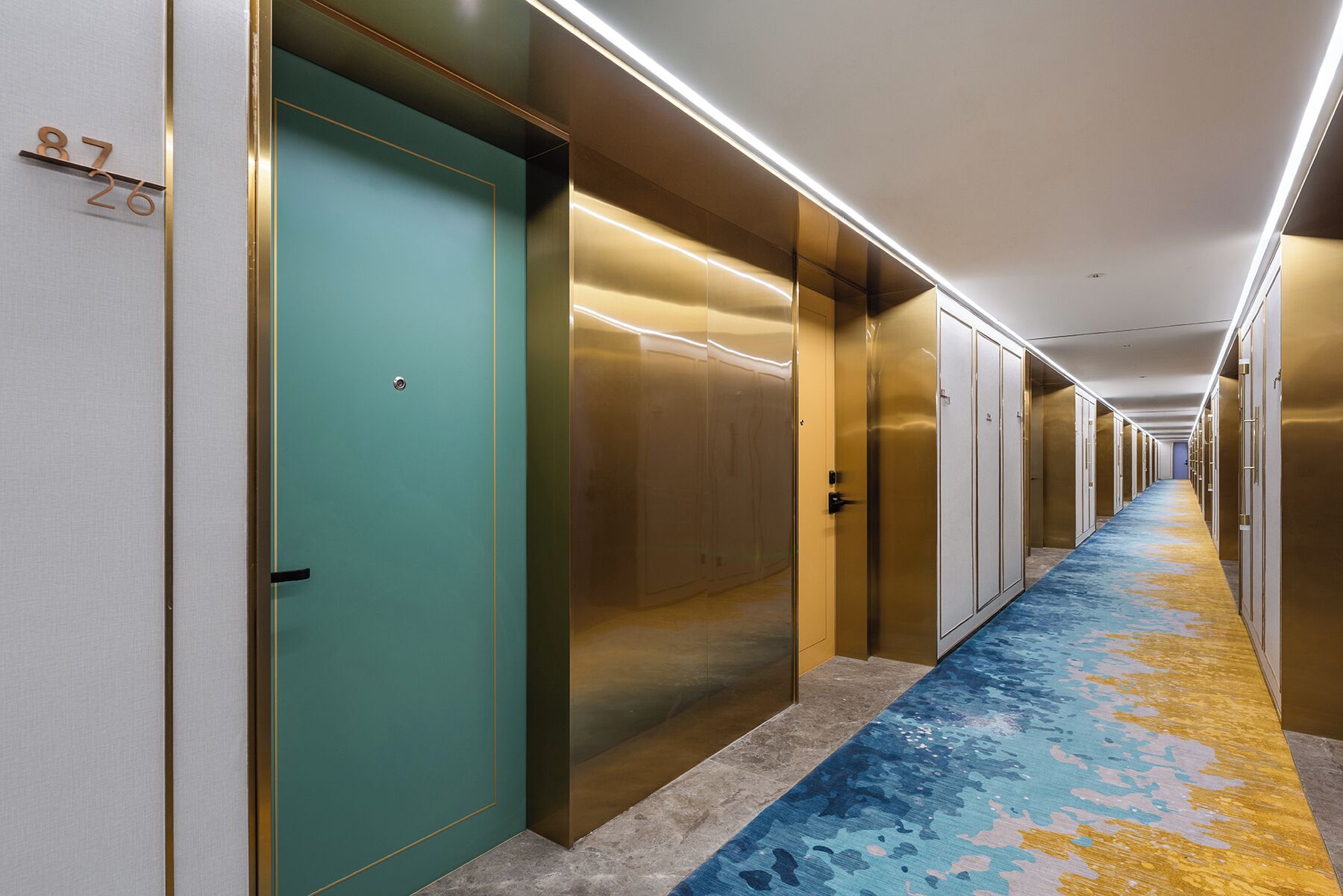 A hotel corridor with doors, a patterned carpet, and a ceiling with linear lighting.