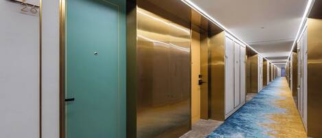 A hotel corridor with doors, a patterned carpet, and a ceiling with linear lighting.