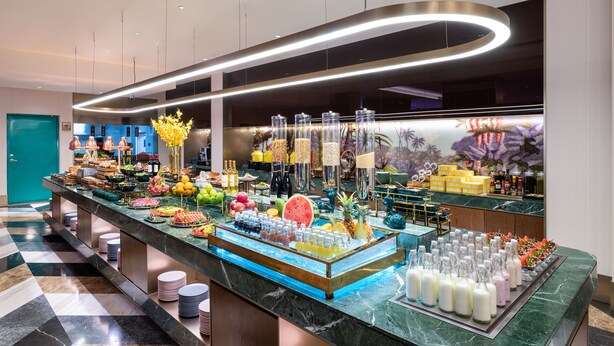 A buffet with various food items and beverages, a teal door, and a checkered floor.