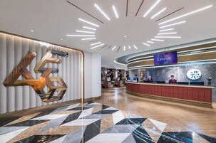 Eine moderne Hotelhalle mit einer Rezeption, einem digitalen Bildschirm und einem einzigartigen geometrischen Wanddesign.