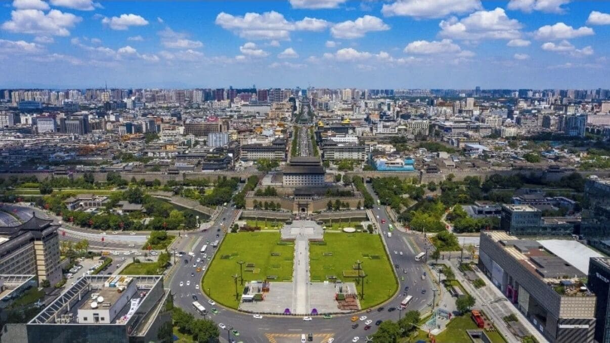 A cityscape with a prominent building in the center, surrounded by greenery and roads.