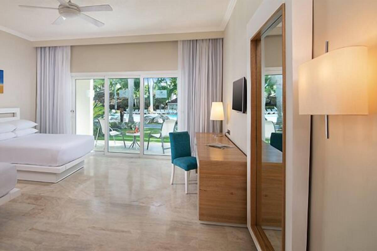 Une chambre d’hôtel avec deux lits, un bureau, une chaise et une grande fenêtre donnant sur une piscine et un espace verdoyant.