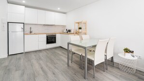 Eine moderne Küche mit weißen Schränken, einem eingebauten Backofen und einem Essbereich mit einem Glastisch und weißen Stühlen.