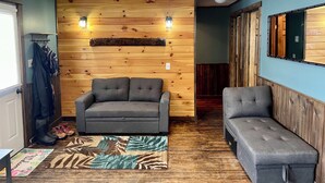 Ein gemütlicher Raum mit einer Holzwand, zwei grauen Sofas, einer Bank und einer Tür mit Kleiderhaken.