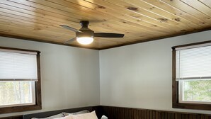 Ein Schlafzimmer mit einem Bett, Holzboden, zwei Fenstern mit Jalousien und einem Deckenventilator.
