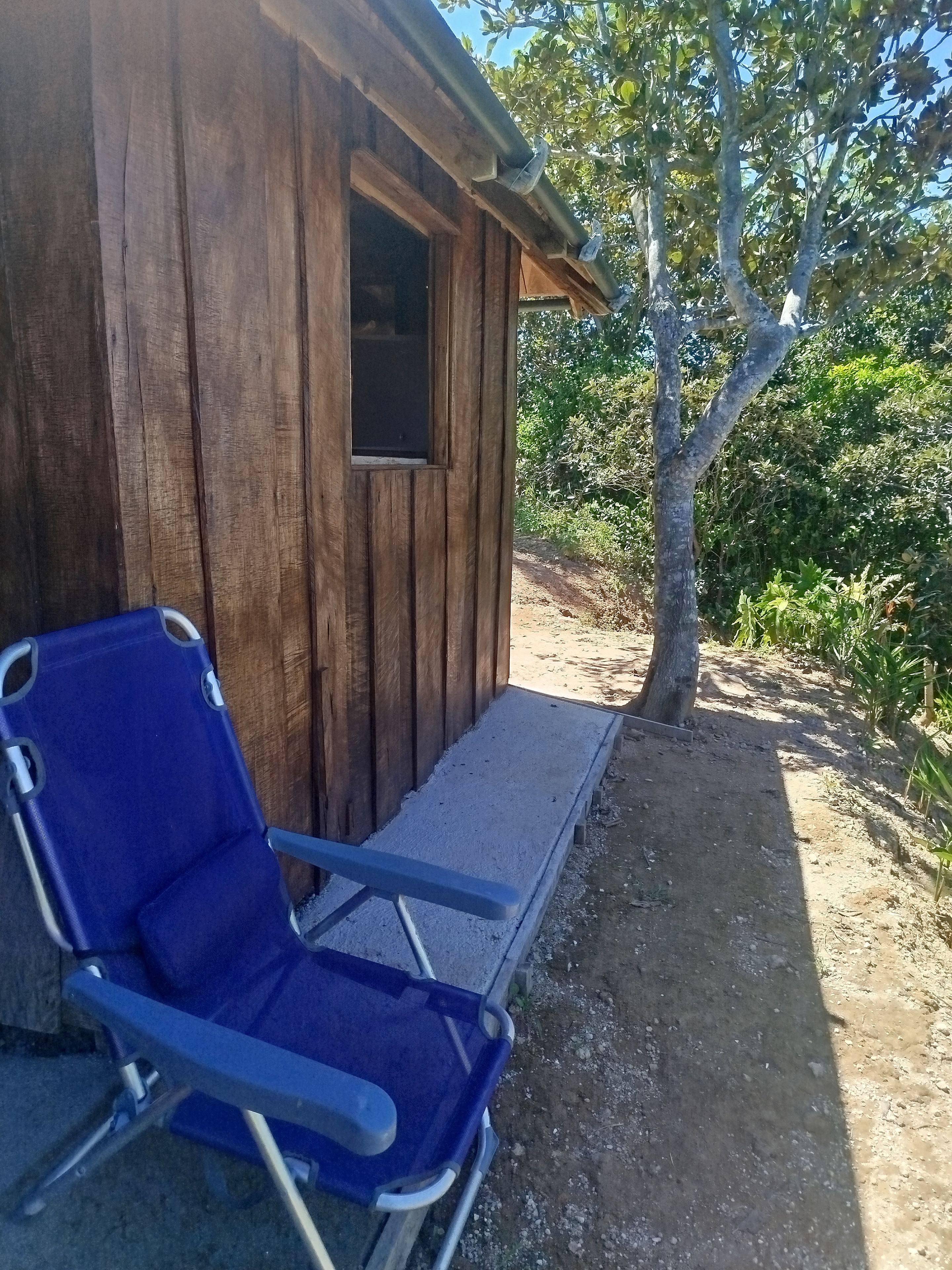 Une cabane en bois avec une seule fenêtre et une chaise bleue à l’extérieur.
