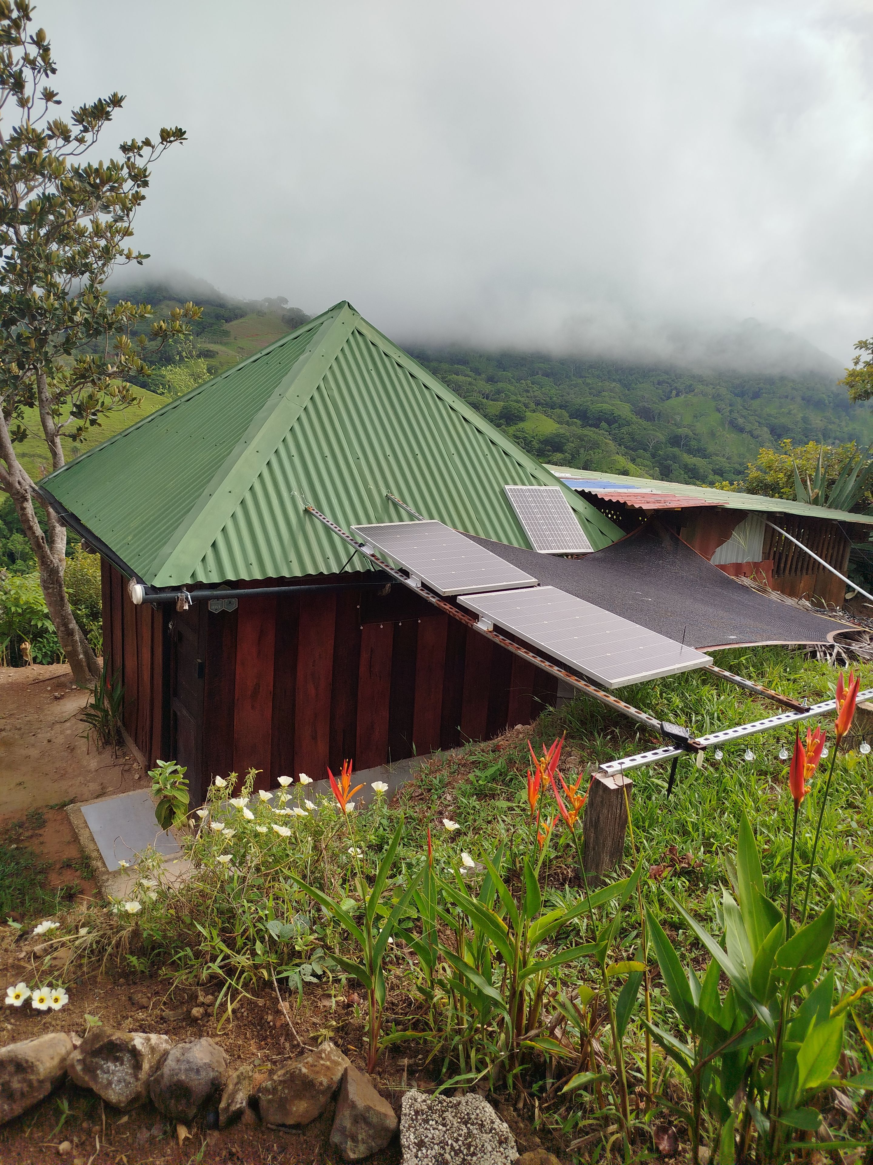 Un edificio rústico de madera con techo verde, paneles solares y vistas a un valle verde exuberante.