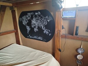 Una habitación con una cama, un mapa del mundo en la pared, un panel de control pequeño y un estante de madera con una linterna.