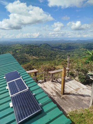 Una azotea con paneles solares, bancos de madera y vistas a un valle exuberante.