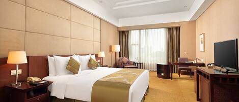 A hotel room with a large bed, a desk with a TV, a chair, and a lamp.