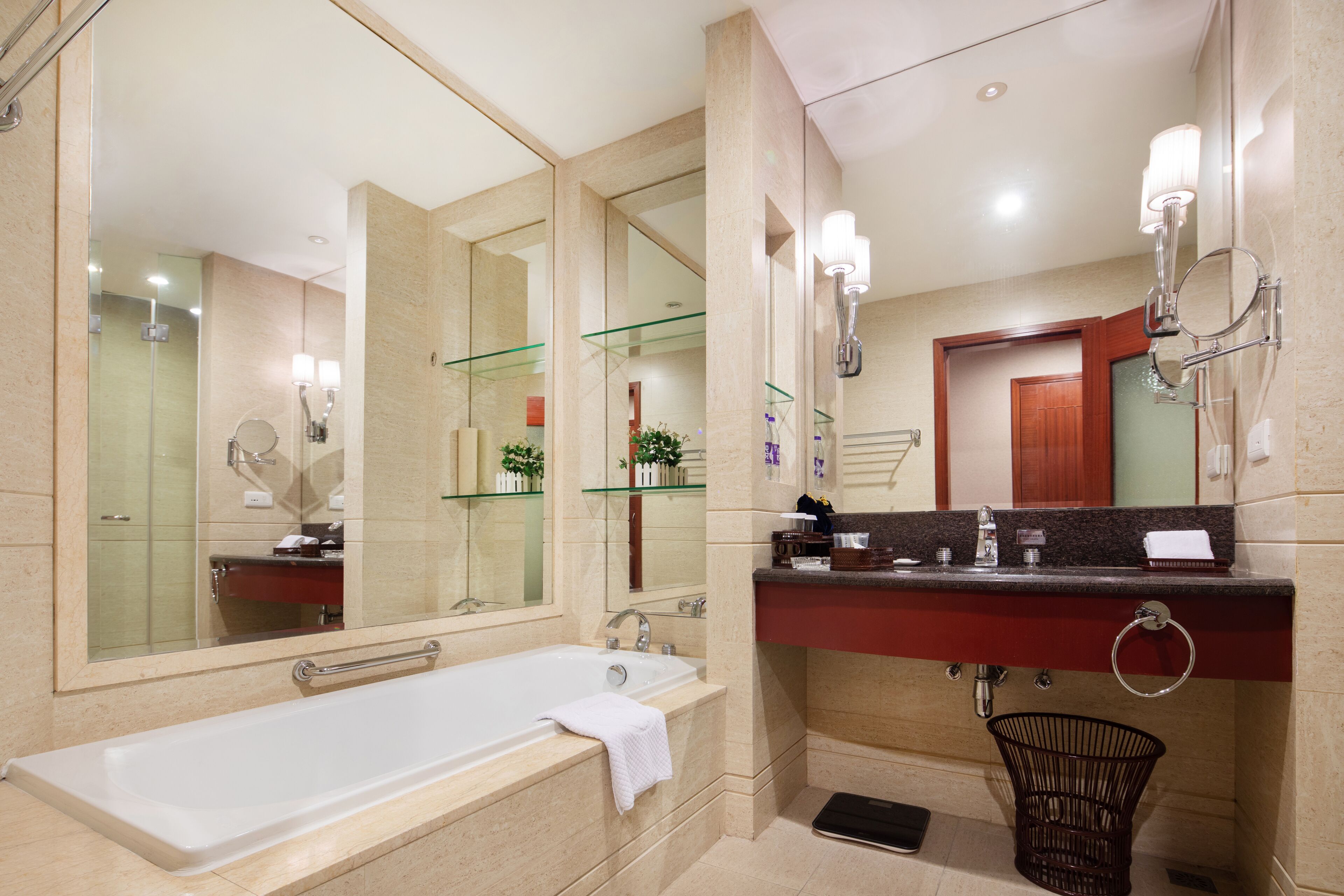 A modern bathroom with a large mirror, a bathtub, a glass shelf, and a sink with a towel ring.