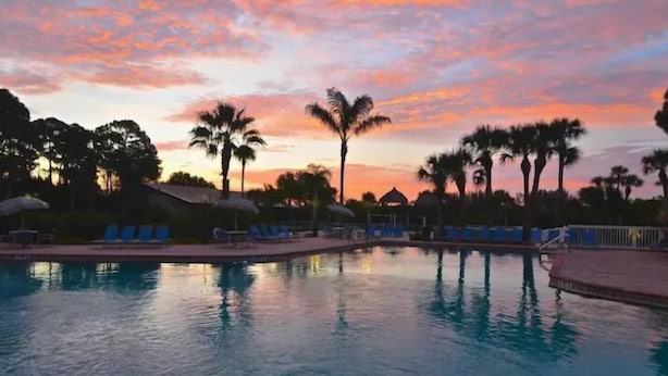 Ein Swimmingpool mit Liegestühlen und Palmen bei Sonnenuntergang.