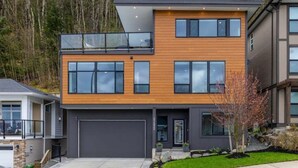 A modern two-story house with a garage, large windows, and a balcony. - A Perfect Mountain Retreat w/ Views, Hot Tub, Home Theatre, Games, PS5 & AC (Chilliwack)
