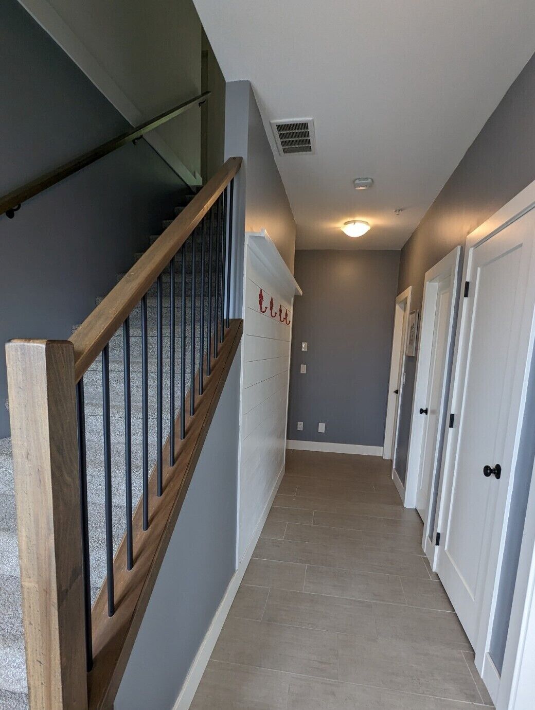 Un pasillo con una escalera de madera, paredes blancas y piso de baldosas.