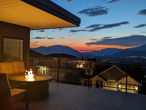 Un balcon doté d’un foyer et de sièges, offrant une vue sur le paysage urbain et les montagnes au crépuscule.