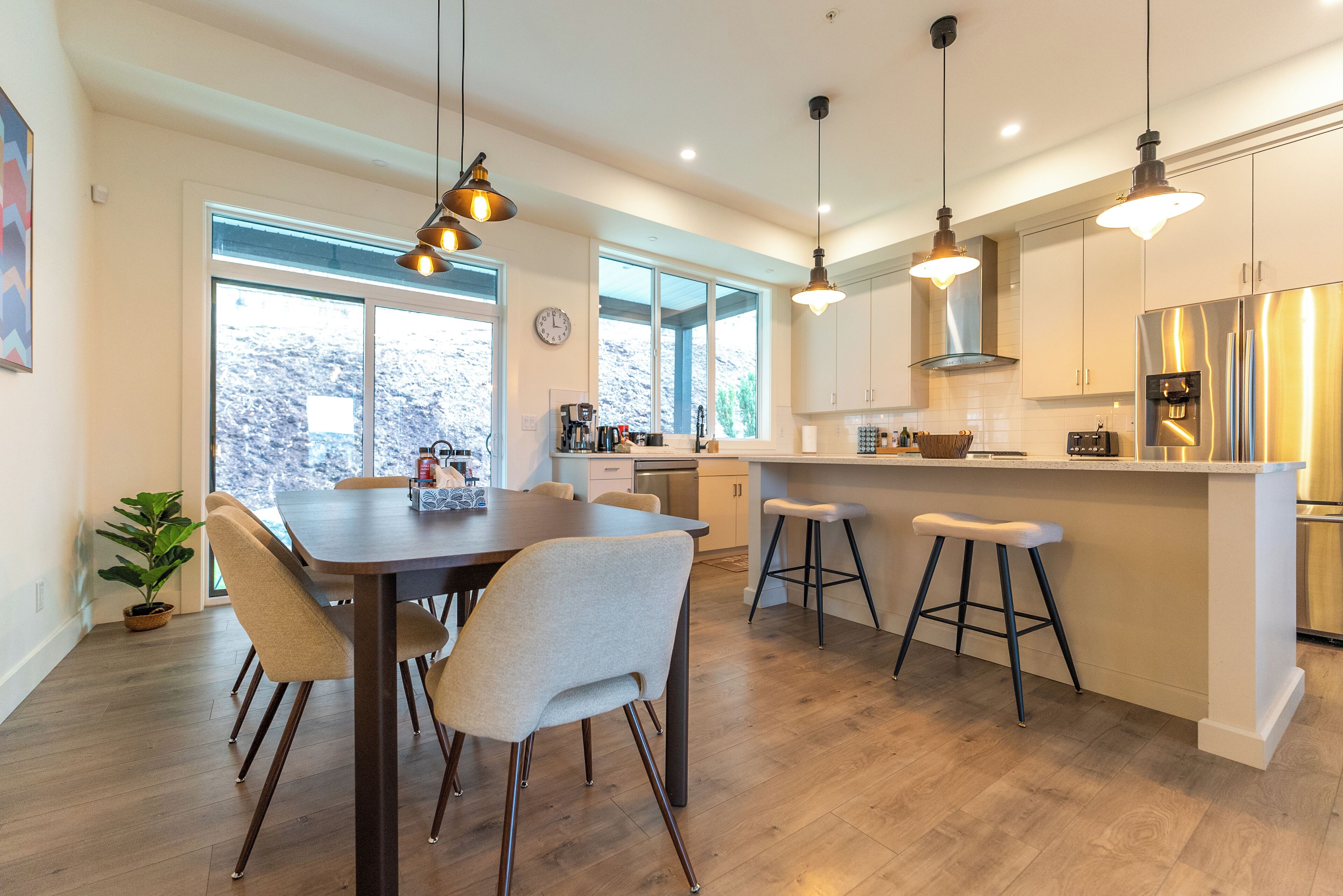 A modern kitchen with a central island, pendant lighting, and a dining area with a wooden table and chairs.
