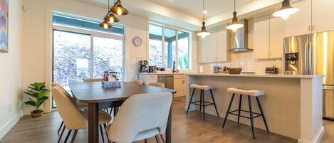 A modern kitchen with a central island, pendant lighting, and a dining area with a wooden table and chairs.