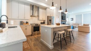 A modern kitchen with stainless steel appliances, a central island with stools, and pendant lighting. - A Perfect Mountain Retreat w/ Views, Hot Tub, Home Theatre, Games, PS5 & AC (Chilliwack)