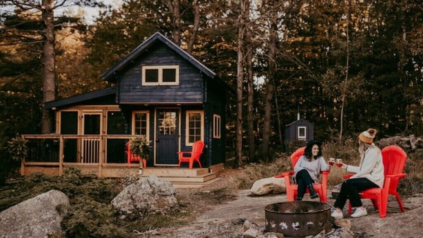 A cabin with a porch, two red chairs, and a fire pit. - Glamphouse Muskoka
 (Gravenhurst)