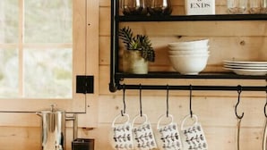 A kitchen with wooden shelves, a coffee maker, and hanging kitchen utensils. - Glamphouse Muskoka
 (Gravenhurst)