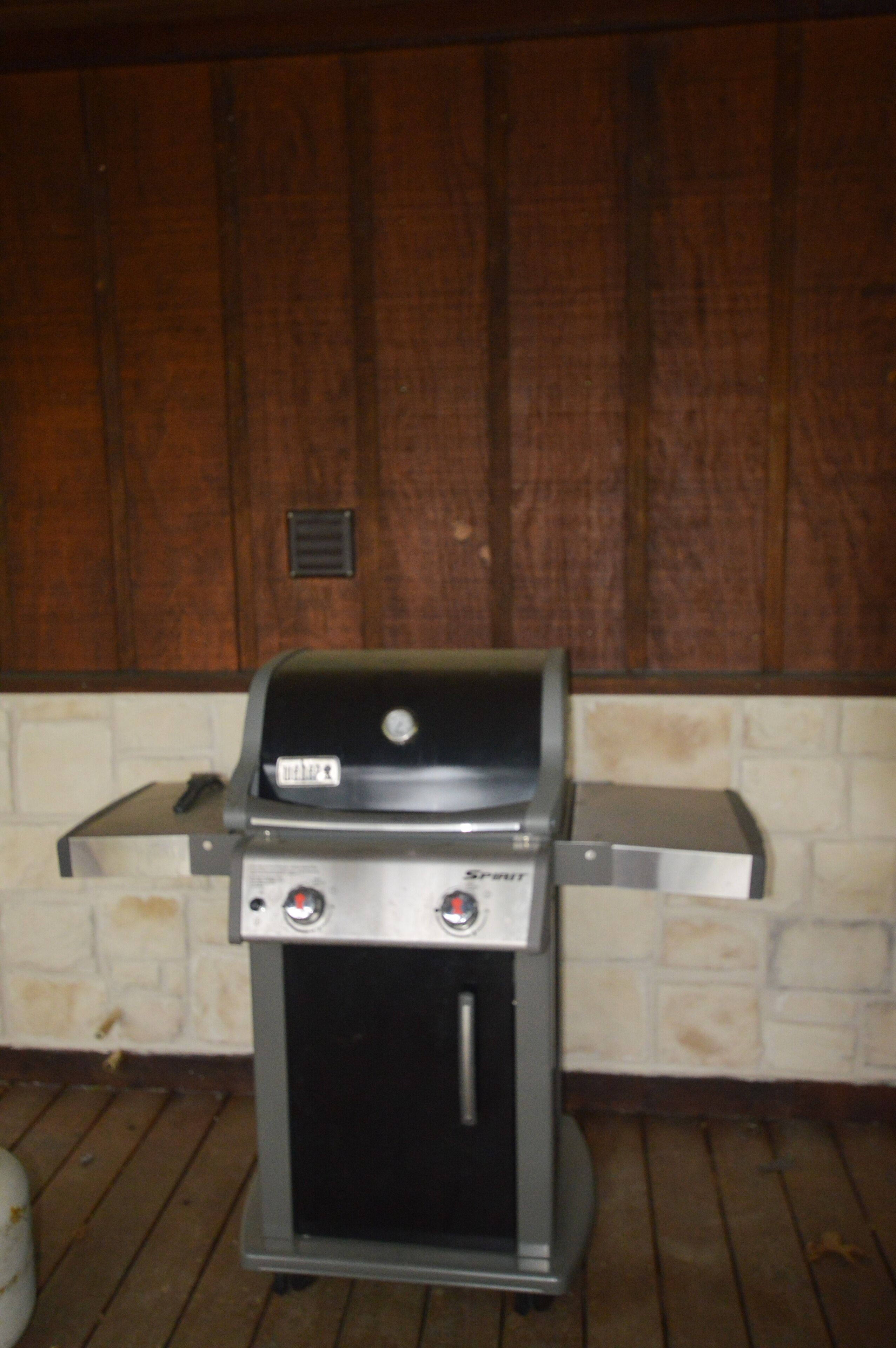 Una parrilla de gas portátil con pantalla digital y dos perillas de control, ubicada sobre una terraza de madera frente a una pared de ladrillo.