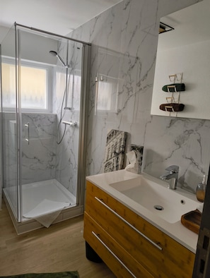 A bathroom with a glass shower enclosure, a wooden vanity, a marble backsplash, and a window. - Apartment 'Haus Auryn' with Private Terrace, Shared Garden and Wi-Fi (Radolfzell am Bodensee)
