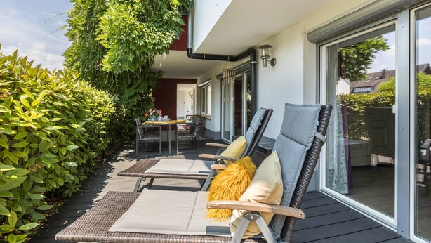 An outdoor deck with lounge chairs, a table, and a glass door leading to a patio area.