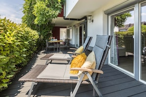 Una terraza al aire libre con sillones de descanso, una mesa y un ventanal de vidrio que da a un patio.