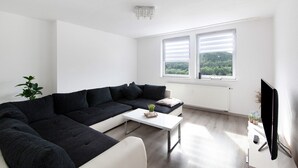 A modern living room with a sectional sofa, a small coffee table, a TV, and a window with a view of greenery. - Apartment 'Zur Nordhelle' with Mountain View and Wi-Fi (Herscheid)