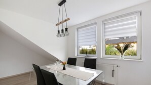A dining area with a table, chairs, a hanging light fixture, and a window with blinds. - Apartment 'Zur Nordhelle' with Mountain View and Wi-Fi (Herscheid)
